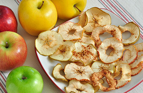 baked apple chips on a plate surrounded by whole apples