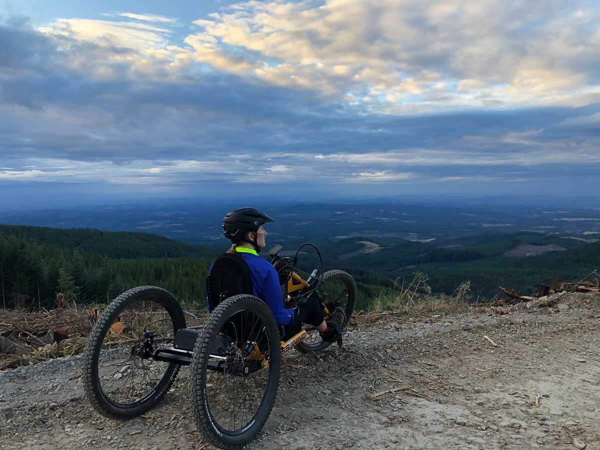 Lizzy sitting in a mountain bike that has 3 tires overlooking a green valley