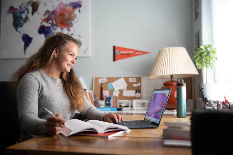 person at a laptop working from a textbook while looking at data on the laptop