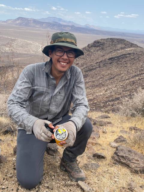 Jose Torres in a desert landscape holding jar of vials