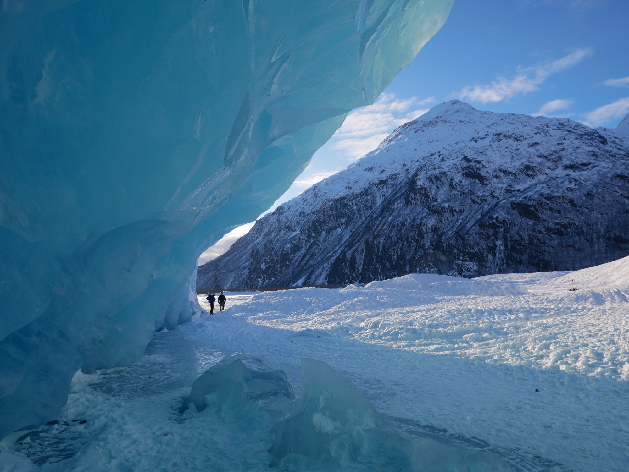 two people standing in between a snowy mountain and a large scale of ice